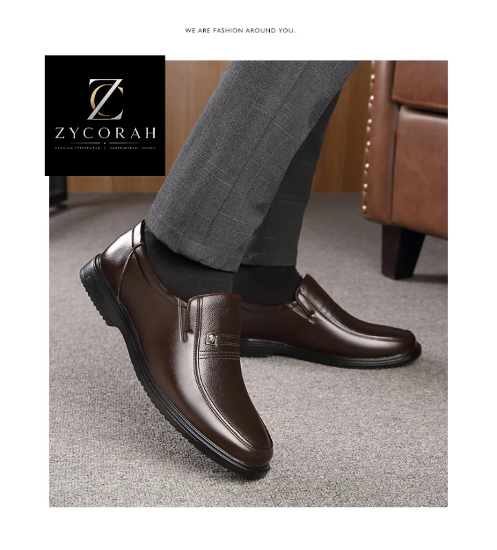 A pair of men's dark brown leather slip-on loafers shown on a model wearing gray trousers and black socks, with a ZYCORAH brand logo overlay in the top left corner.