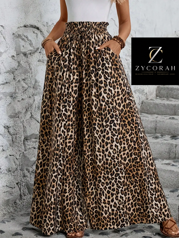 A model wears high-waisted, wide-leg leopard print pants with a white top and brown sandals, standing against a textured gray stone wall. A black brand overlay for 'ZYCORAH' is visible in the upper right.