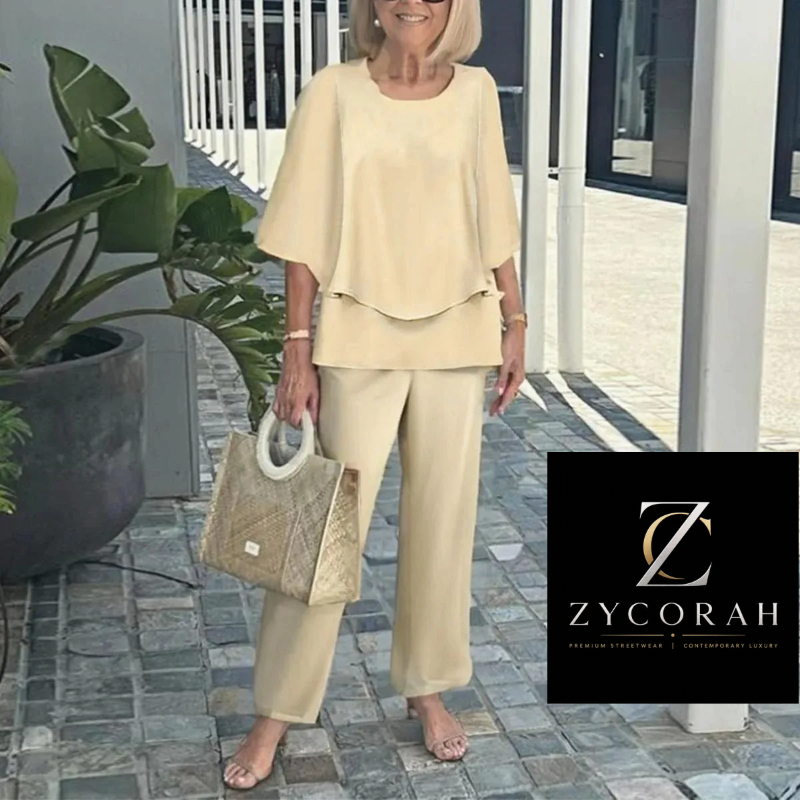 A woman modeling a light beige two-piece lounge set consisting of a short-sleeve top and matching wide-leg pants, holding a woven handbag. A black brand logo overlay for 'Zycorah' is visible in the bottom right corner.