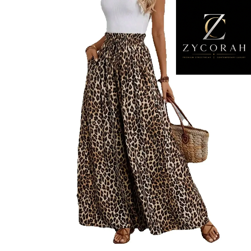 A woman models a pair of wide-leg leopard print maxi pants with an elastic waistband, paired with a white ribbed top and brown sandals. She is holding a woven straw handbag.