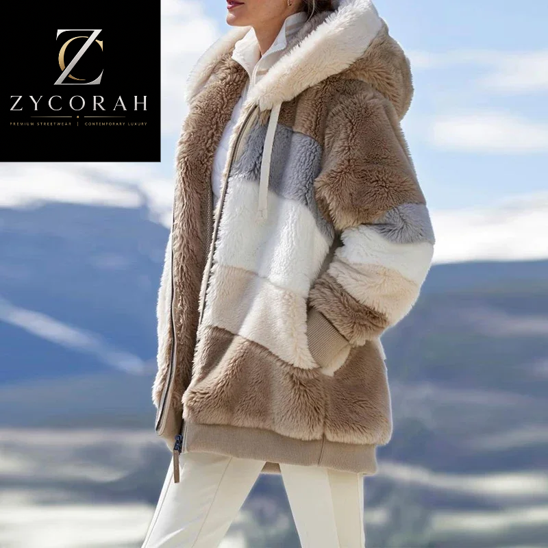 A woman wearing a plush faux-fur hooded jacket with large color-blocked panels in taupe, cream, white, and light gray, photographed outdoors against a blurred mountain landscape. The Zycorah logo appears in the top-left corner.