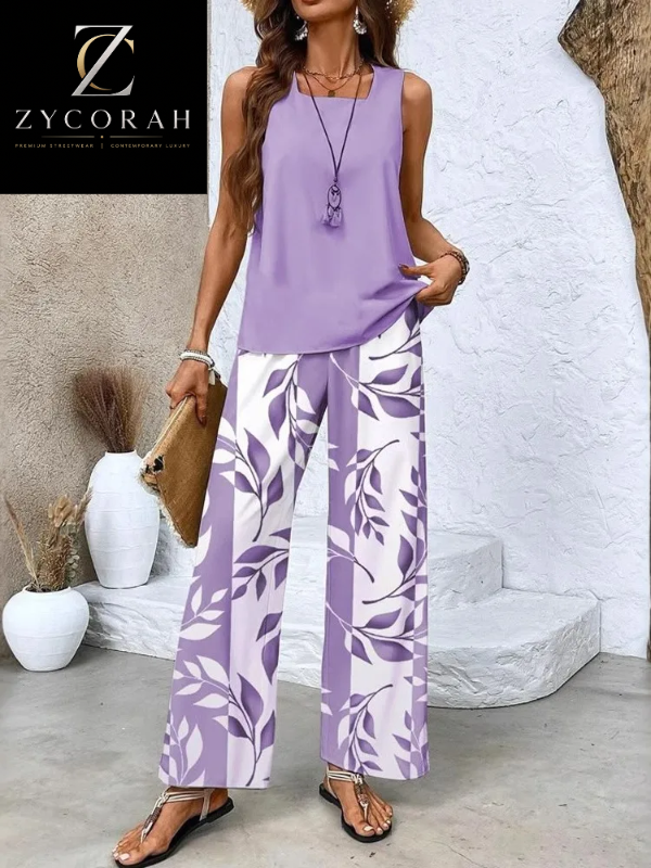 A woman models a sleeveless lavender top and matching wide-leg pants with a white and lavender leaf pattern, styled with a brown clutch and sandals in an outdoor patio setting.