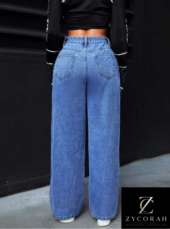 A person shown from the back wearing high-waisted, wide-leg blue denim jeans with a black cropped long-sleeve top. The photo is taken against a dark wall, with a Zycorah brand logo overlay in the bottom right corner.