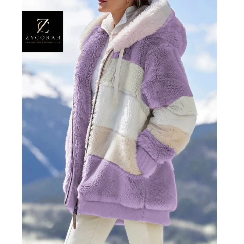 A woman wearing a plush hooded jacket with color-blocked panels in lavender purple, cream, and beige, photographed outdoors against a blurred mountain landscape. A ZYCORAH logo appears in the top-left corner.