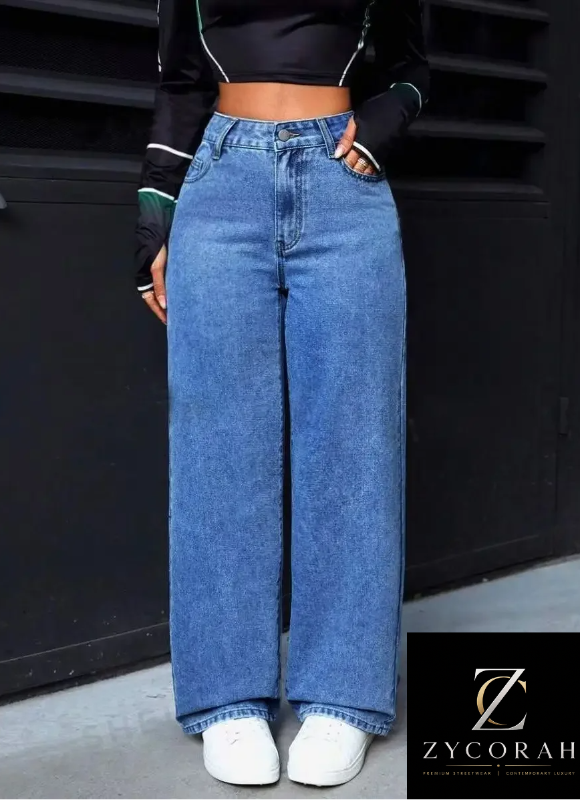 A person wearing high-waisted, wide-leg blue denim jeans with a black cropped long-sleeve top and white sneakers, standing in front of a dark paneled wall. A ZYCORAH brand logo card is visible in the bottom right corner.